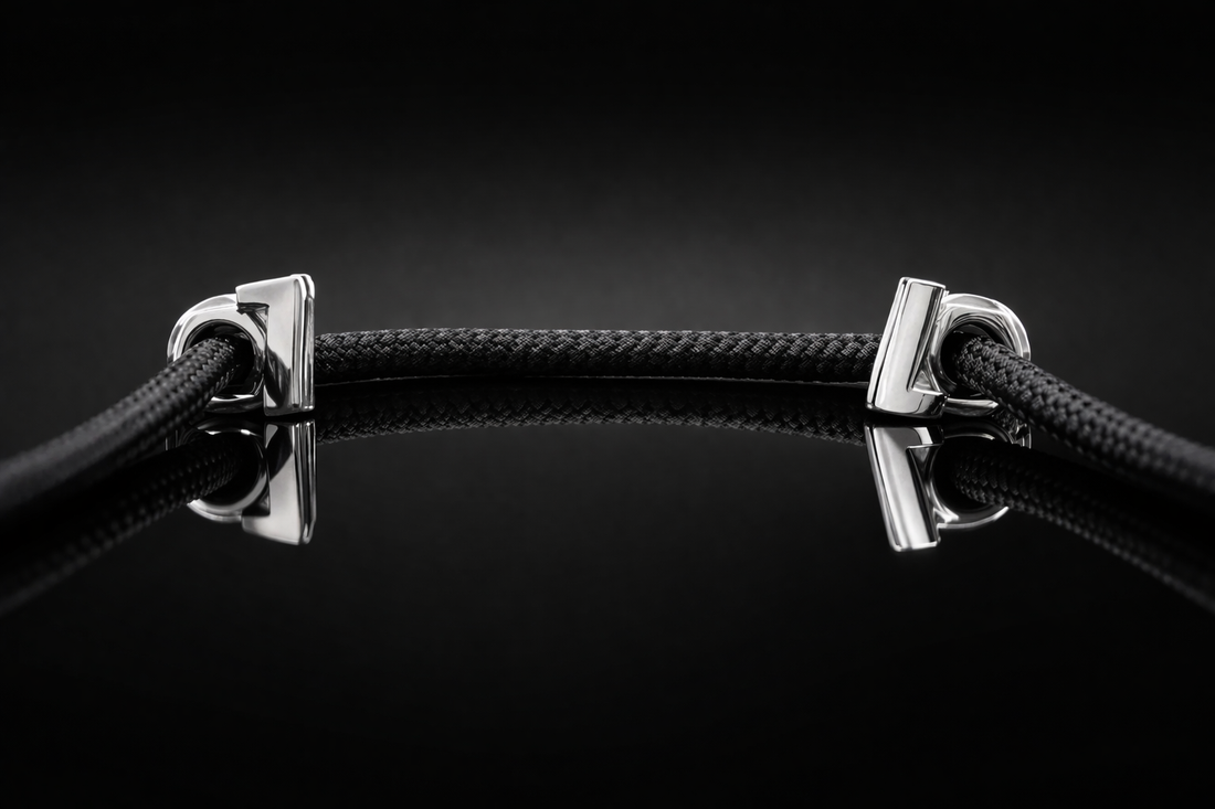 Black braided shoelace with polished metal aglets threaded through sleek eyelets, displayed on a glossy black glass surface with a subtle mirror reflection and dark gradient background, emphasizing precision, luxury, and material contrast