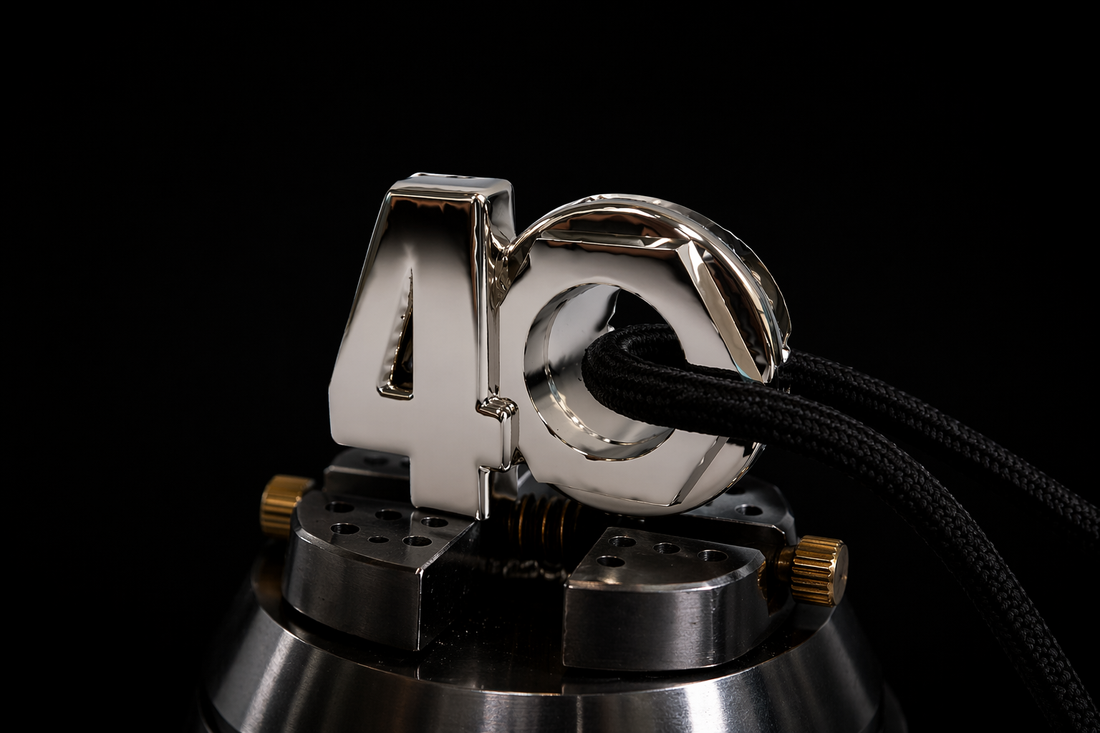 Black shoelace with aglet threaded through an octagonal metal eyelet in a polished silver “40” pendant, secured on a precision jewelry vise against a dark luxury background.