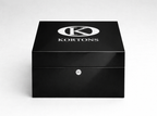 Closed glossy black KORTONS eyelet box with centered logo and front lock detail, presented in a clean studio setting to emphasize luxury footwear hardware packaging.