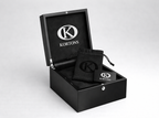 Open KORTONS luxury eyelet box with glossy black exterior and suede interior, featuring a black drawstring pouch and branded card inside, presented in a clean studio setting.